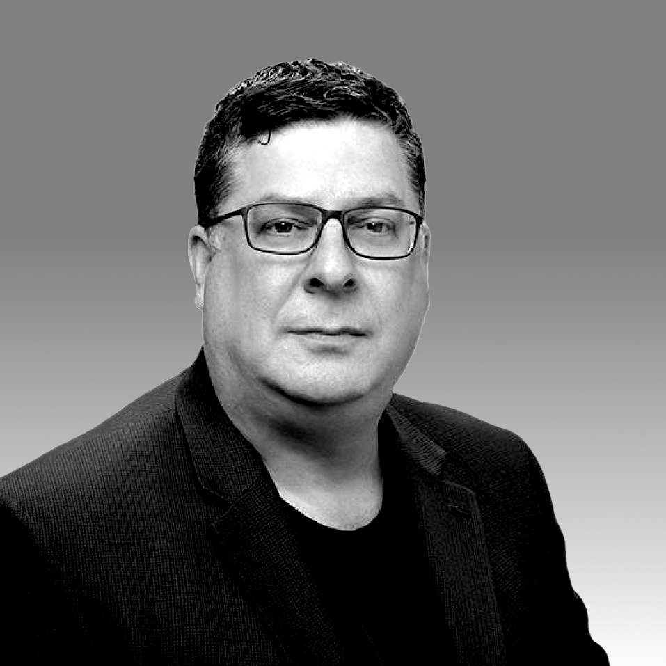 Portrait of Keith with dark hair, wearing a dark shirt, suit jacket, and glasses.