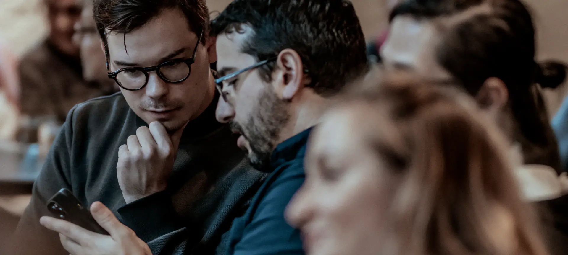 Closeup of group of employees sitting during a speaking engagement. Two men looking at smart phone.