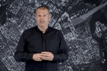 Man wearing a black collard shirt standing in front of SAR Data imagery