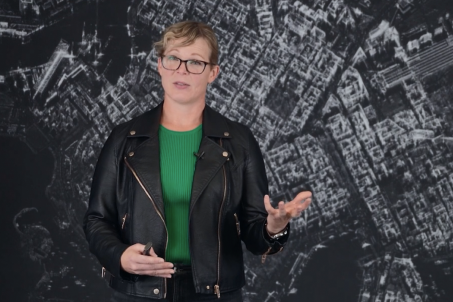 Woman wearing glasses, green shirt, and black jacket standing in front of SAR Data imagery